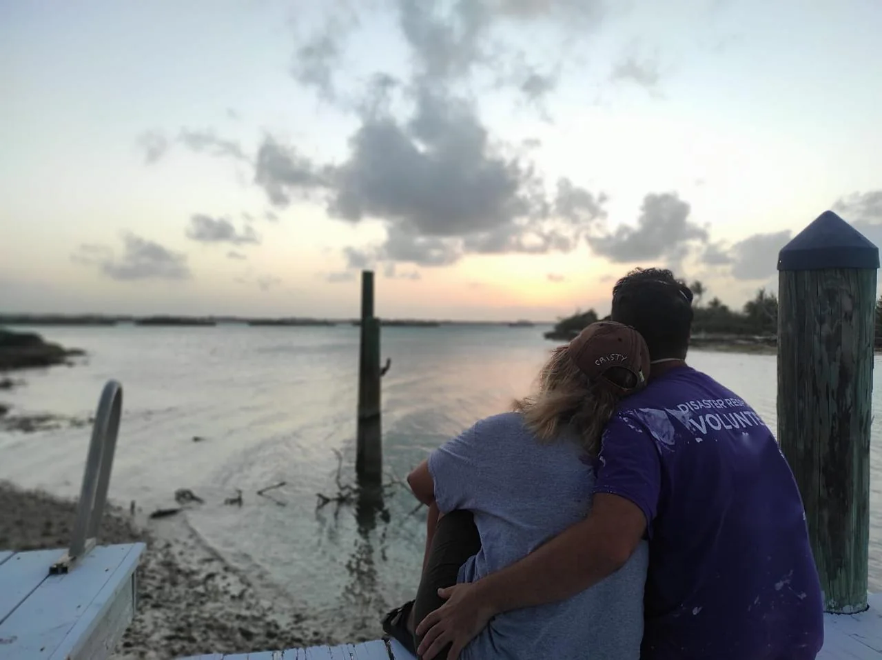 Cristy y Ted sentados en un muelle en Bahamas al atardecer, con camisetas de voluntarios